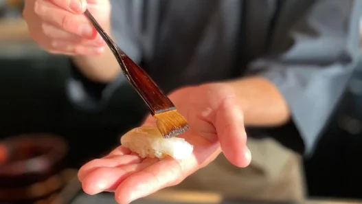 a person holding a brush over a sushi