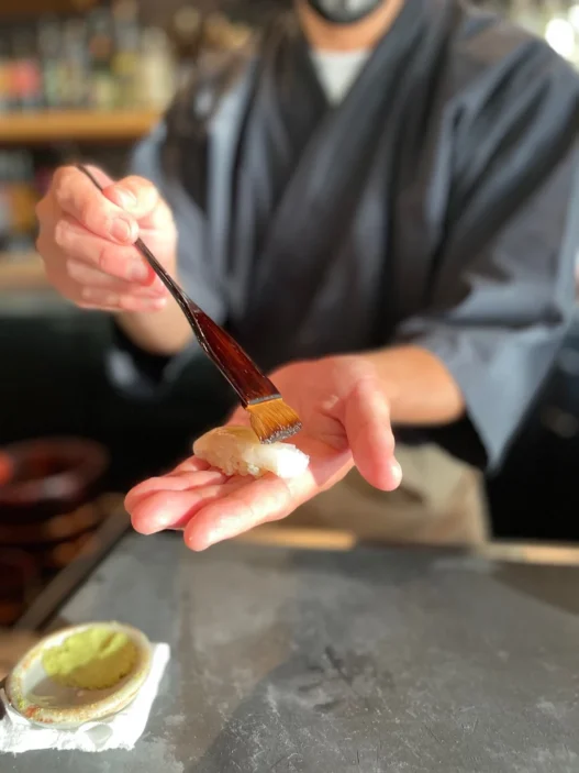 a person holding a brush over a sushi
