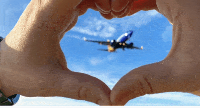 a hand making a heart with a plane in the sky