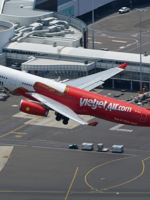 a red and white airplane flying over a runway