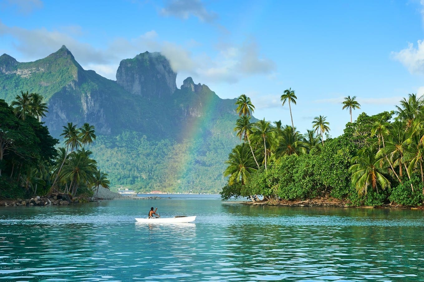 a couple in a boat on a body of water with trees and mountains in the background